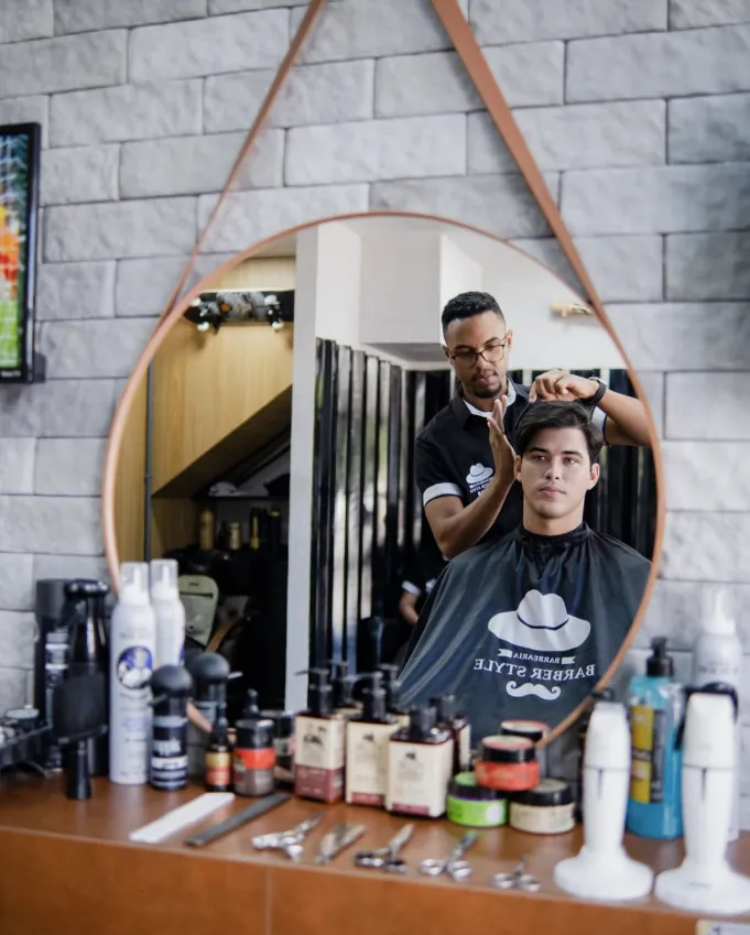 Barbeiro finalizando um corte refletido no espelho redondo